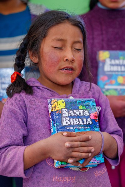 A girl prays holding her new Bible.